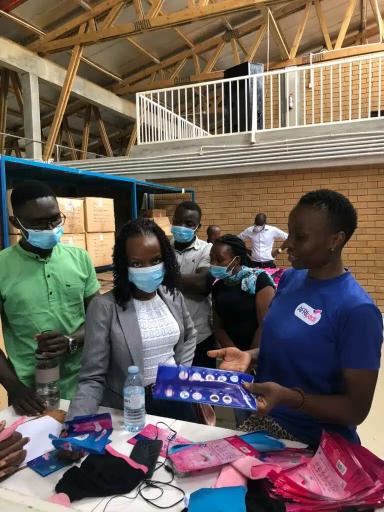 Medical Research Council looks on as AFRIpads factory worker showcases AFRIpads Menstrual Kits. 